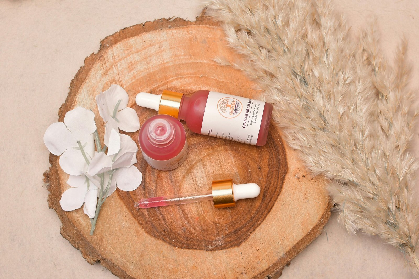 Aesthetic flat lay of cosmetic serum bottle with pampas grass and flowers on a wooden slice.