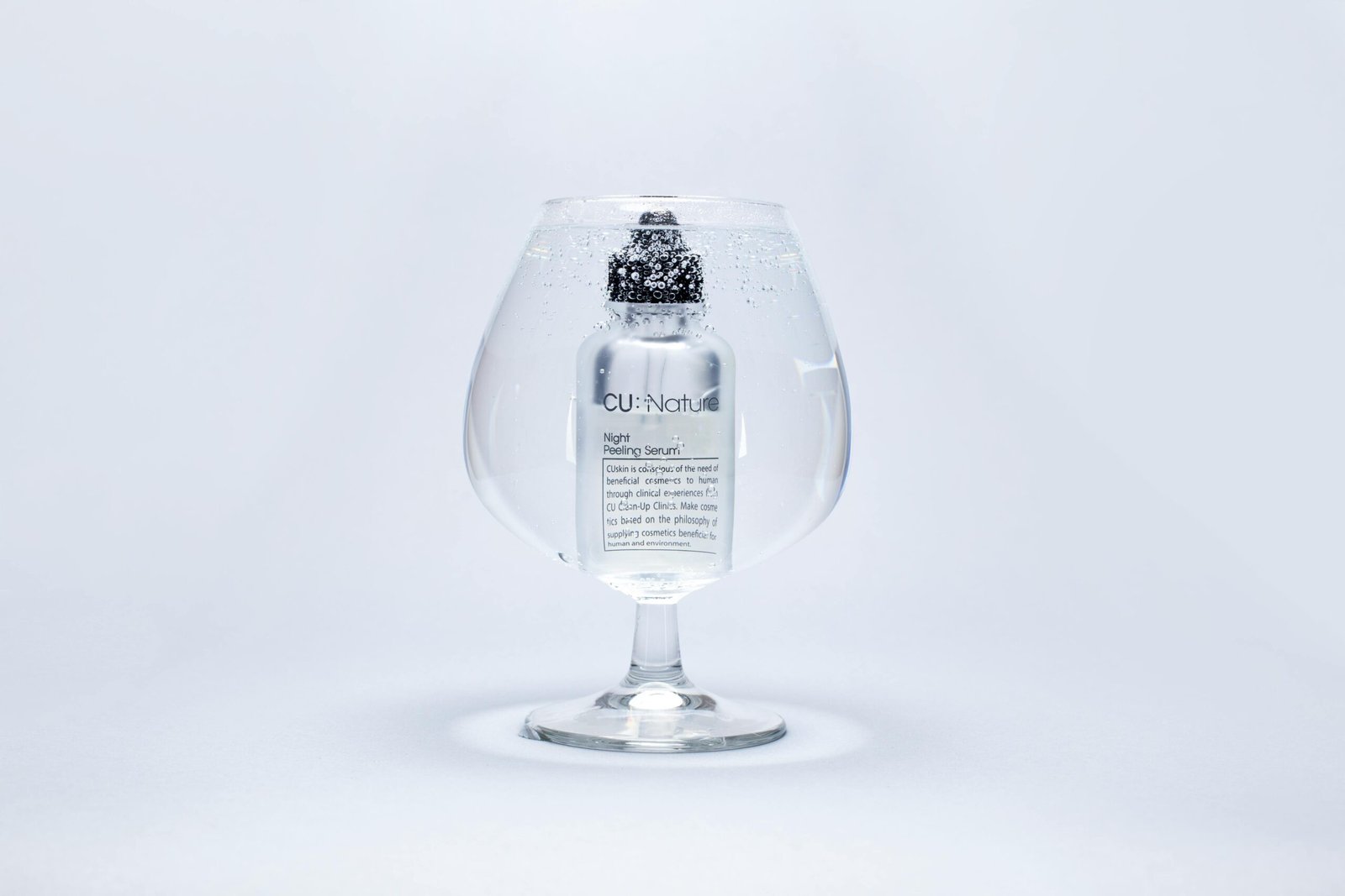 A luxury serum bottle submerged in a large wine glass filled with water, showcasing purity and elegance.